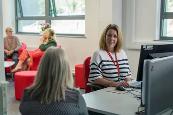 two members of the faculty of business and creative industries team having a conversation at a desk, smiling