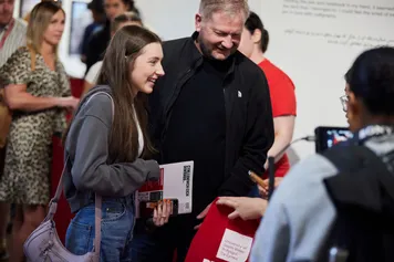 A prospective student with their parent smiling and talking to a lecturer