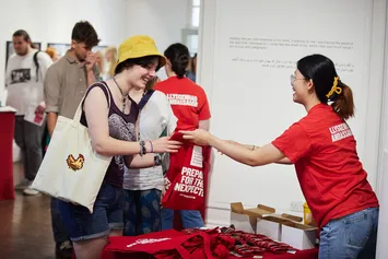A student ambassador is handing out a USW tote bag at an open day.