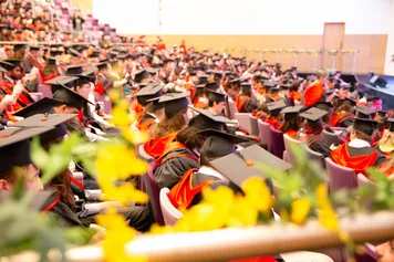The auditorium of Newport's ICC packed with students dressed in graduation gowns and caps watching their graduation ceremony