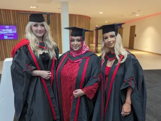 three network75 students at graduation wearing graduation robes and hats all smiling to camera