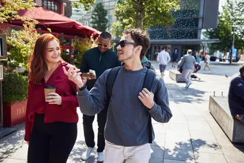 Two students smiling in the sun walking through Cardiff city centre.