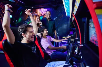 A group of students celebrating over winning a racing car game at an arcade bar.