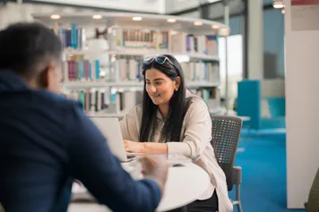 two students working togther at a desk in the Newport Campus Library