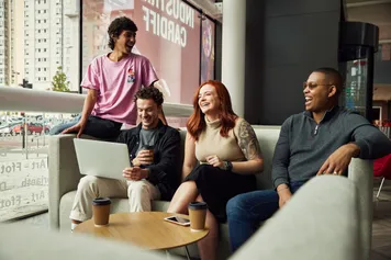 A group of students laugh while discussing work over a laptop at the Cardiff Creative campus