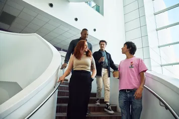 Four students walking down a spiral staircase and talking to eachother.