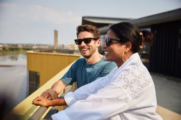 Two students wearing sunglasses and overlooking the river usk from the rooftop garden at the Newport Campus.