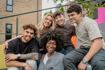 A group of students are sat together on colourfully painted steps outside the Treforest campus accommodation buildings.