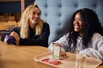 Two students sat in stilts smiling over food