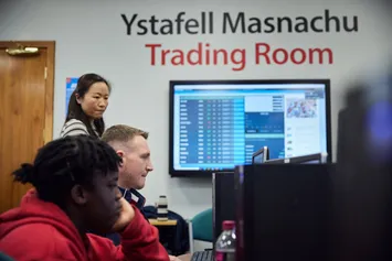 Lecturer surveying students in the Trading Room, accounting data is displayed on the classroom board.