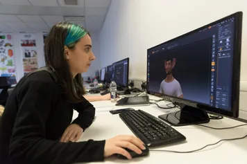 student in classroom using computer and looking at screen with a cgi visual of a man on screen