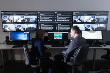 Two policing lecturers sat discussing in front of the screens in the hydra simulation centre on glyntaff campus