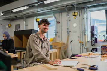 An interior design student sat in a workshop room with tools on the tables, smiling.