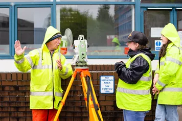civil engineering students in high vis jacket outdoors, next to equipment set with windows behind them