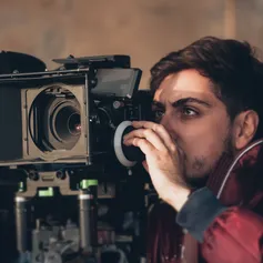 A close up of somebody looking into a large film camera while adjusting a dial on the side