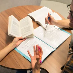 A close up of two students holding books and writing notes while discussing their work