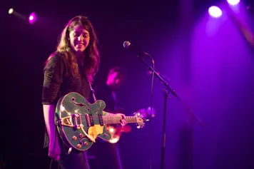 A student on stage standing at a microphone with a guitar.