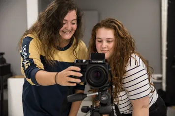 Two students are working together using a tripod and camera.