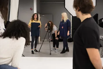 A lecturer is supervising a lesson, while students set up a professional photoshoot.