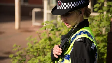A student police officer in uniform is talking into their shoulder radio.