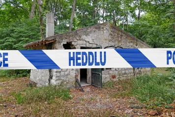 Abandoned stone house in the woods with a police tape with written in it in Welsh 