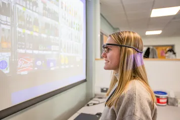 A student is taking part in a class activity. They are wearing a pair of technological glasses which is recognising images on a screen.