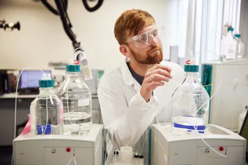 A student in lab uniform is working with various liquids and lab equipment.