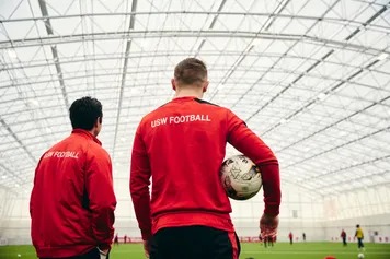 Two football coaching students looking out onto a indoor football pitch.