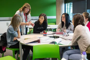 A lecturer is talking to a group of students sat around a table in the primary teaching classroom at the USW Newport campus.