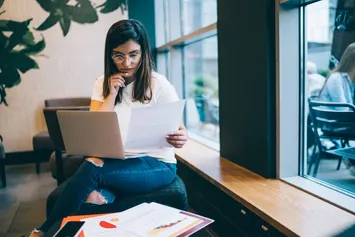 A student reading of her application form with a laptop resting on her knee