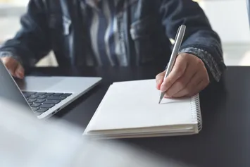 Student using a laptop and taking notes on paper