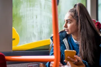 A student sat on a bus looking out the window while on her phone