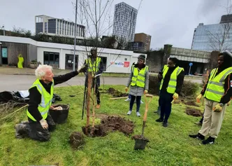A group of people in hi-vis jackets planting trees outside the Stiwdio at Cardiff Campus.