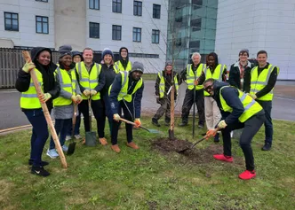 A group of people in hi-vis jackets holding shovels and smiling after planting trees at the Cardiff campus.