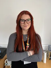 Hannah Cord-Jenkins yn sefyll gyda'i breichiau wedi'u croesi yn gwenu ar y camera