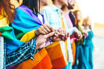 Group of people holding hands, draped in rainbow flags