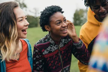 A close-up on a group of friends smiling and chatting while sat on the grass in a park