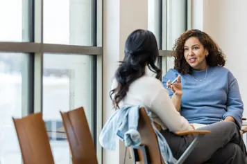 Two adults talk sincerely while sat in private on two chairs in a canteen setting