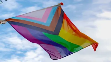 The inclusive and progressive LGBTQ+ Pride flag flying against a blue sky