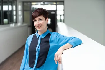 Lecturer Dr Thania Acaron leans on a white banister while wearing a blue shirt inside USW's Cardiff Campus