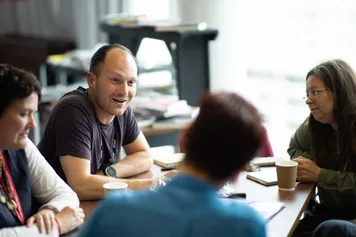 A group of researchers sit around a table chatting with coffee and books