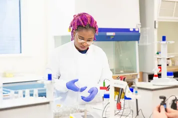 Postgraduate student Talatu Usar conducts an experiment with a pipette in a science laboratory while wearing a lab coat and blue medical gloves