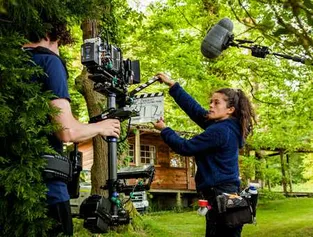 Two people filming in front of a cabin in the woods