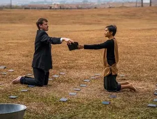 Two men kneeling in a field passing an object between them