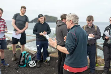 A group of students listening to an academic talk on a geology field trip.