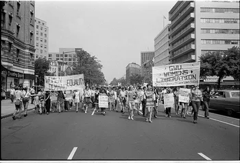 An old black and white photo of a large group of women marching through the streets of Cardiff calling for equality. They are carrying small placards as well as two big banners - one banner says 