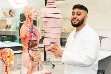 A medical sciences student stood in a lab with an anatomical model.
