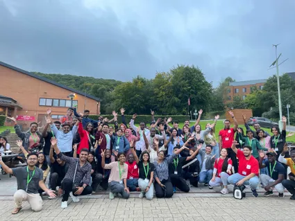 A large group of students smiling at the camera with their hands in the air at international welcome programme