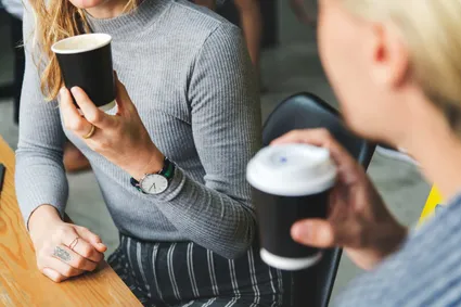 two people sitting at a table drinking coffee from take away cups