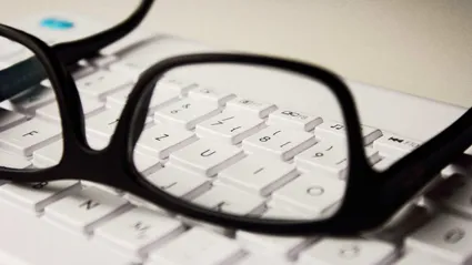 A pair of black framed glasses laying on a computer keybaord